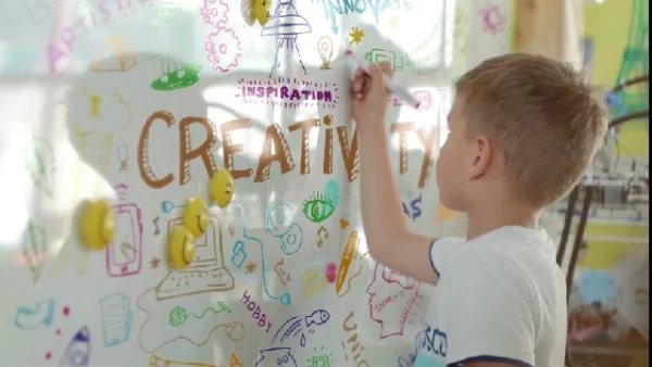 Child writing among colorful words and drawings on a writable wall surface.