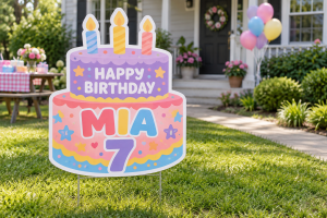 Colorful cake-shaped Happy Birthday Mia yard sign with candles displayed on a lawn.